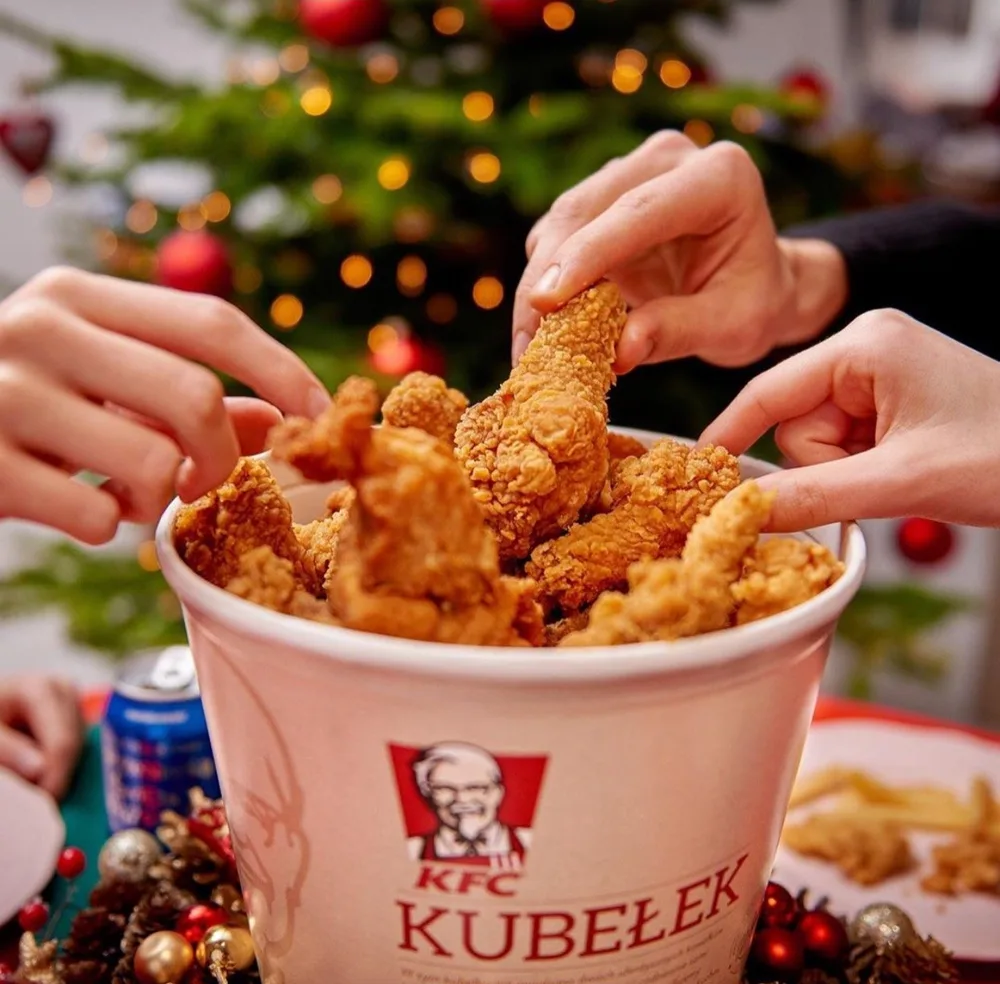 Dłonie sięgające po kurczaka z kubełka KFC przy choince